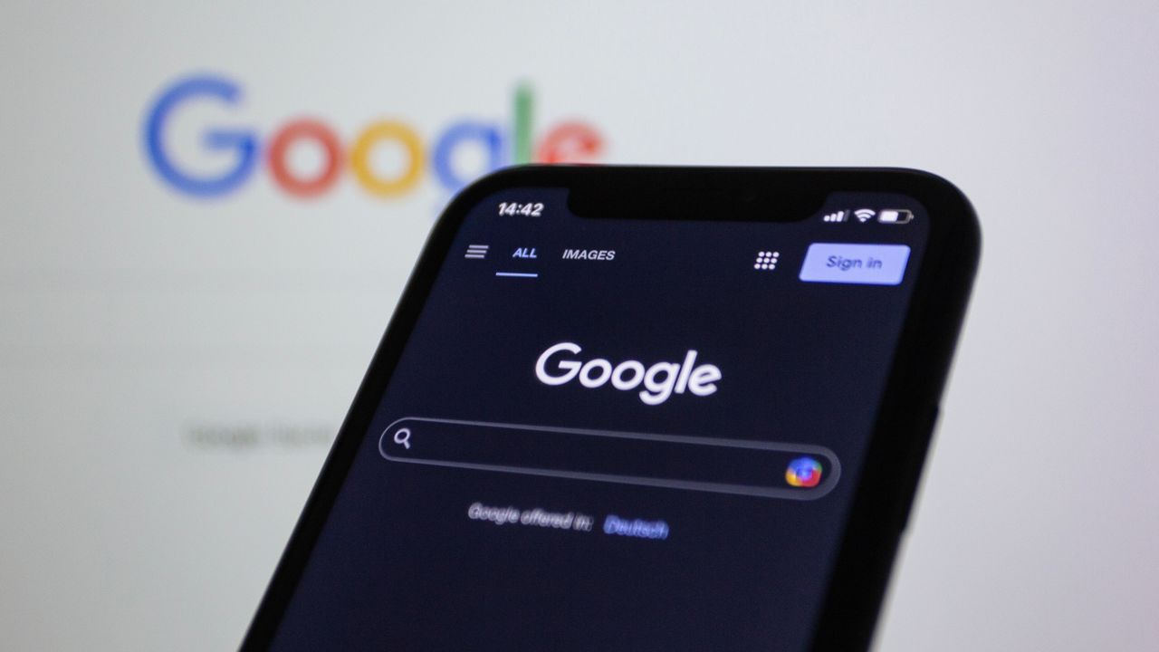 Écran de smartphone affichant une recherche Google en mode sombre, avec le logo Google en arrière-plan.